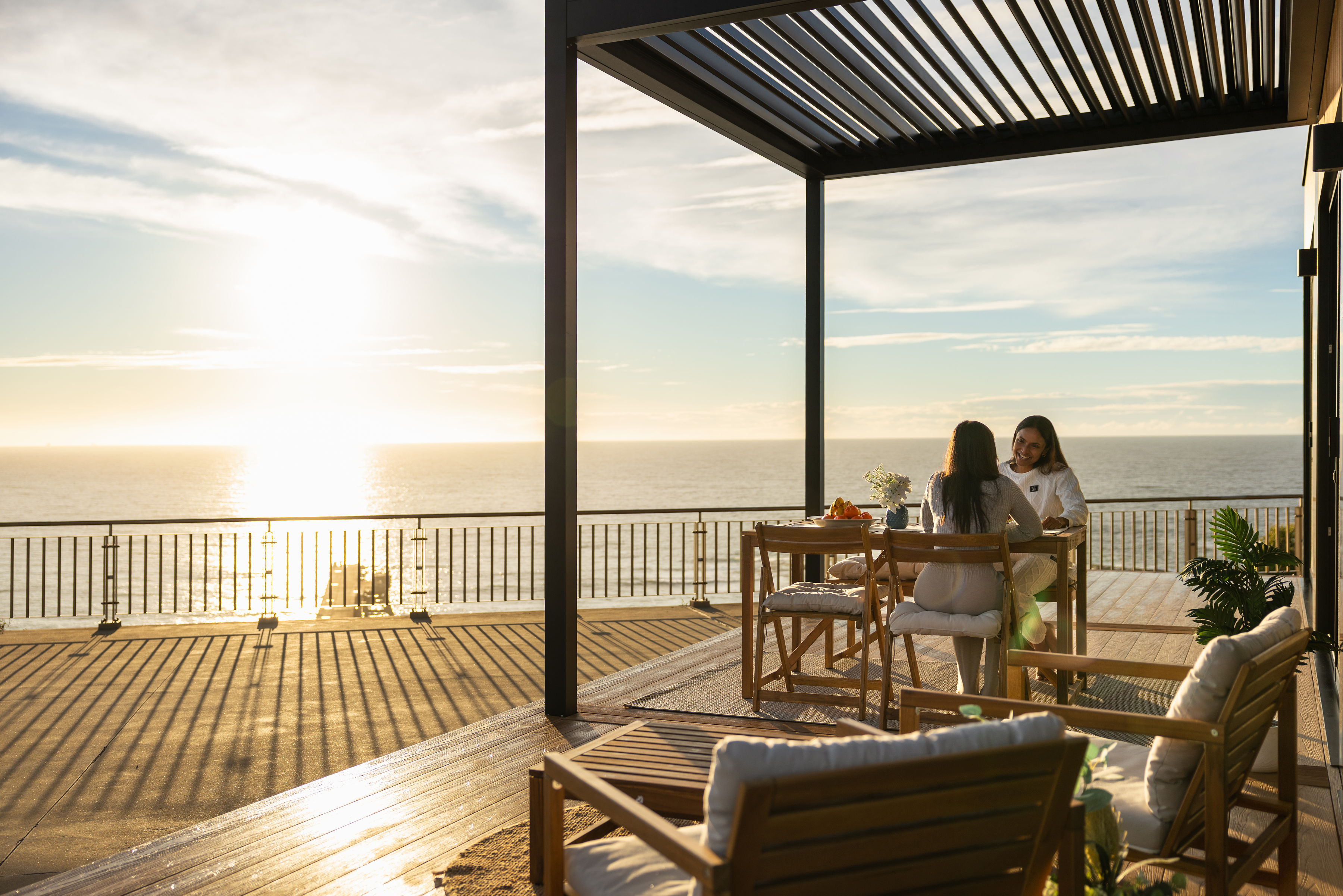Two people at the OHOME terrace table above the ocean at sunset